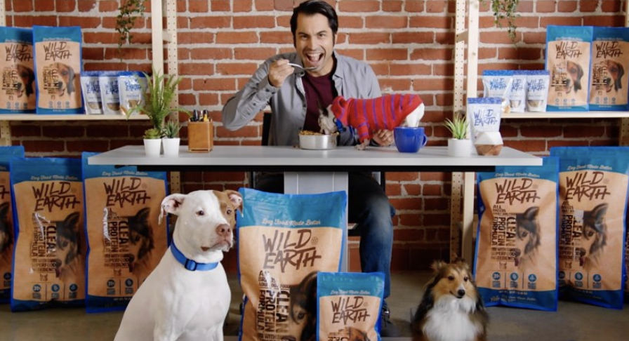 Man eating pet food behind two dogs and many dog food bags