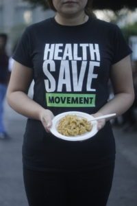 Torso of a woman holding a plate of food and wearing a T-shirt with the words "Health Save Movement"