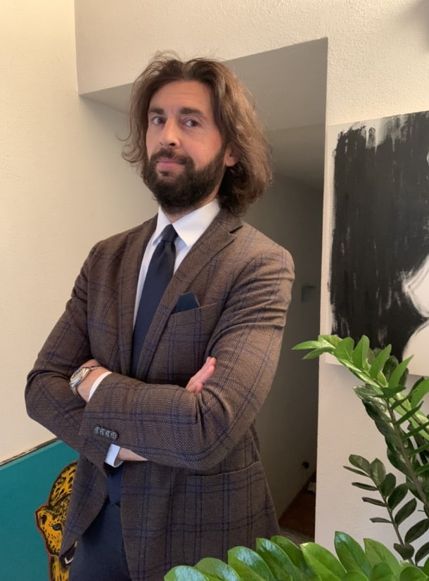 Long haired bearded man in a suit looking at the camera with his arms crossed