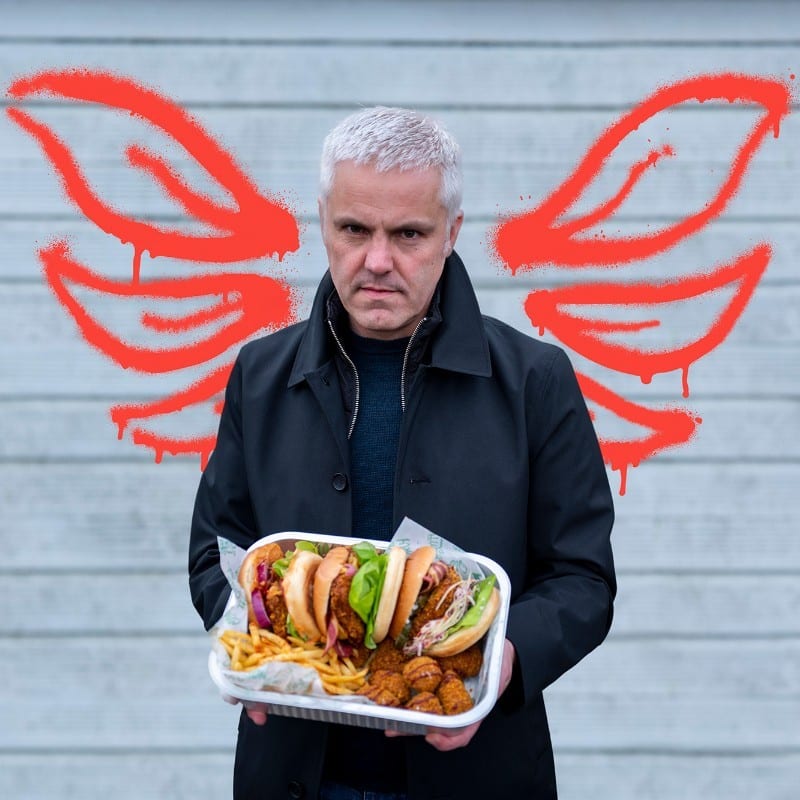 Man holding some food, in fron of a wall with two red angel wings