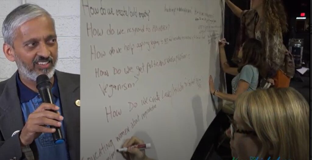 Man talking in a microphone, and someone writing on a board