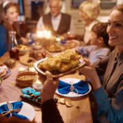 Happy woman passing food to her husband during family dinner on Hanukkah. By Drazen,
