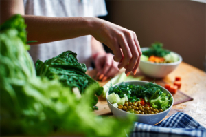 Green onions in a bowl with green peas, cucumbers, carrots, lettuce and dill standing on a table. 
