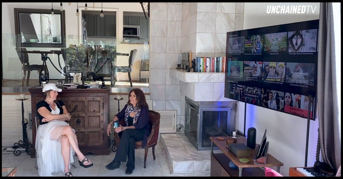 Jane Velez-Mitchell sits beside a large screen displaying UnchainedTV programming.